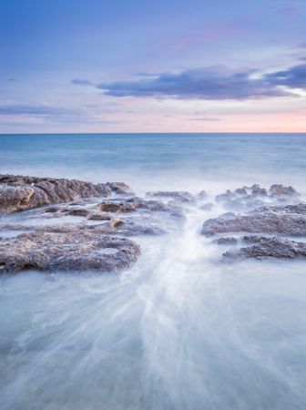 Sea waving near rough rocks during sunset