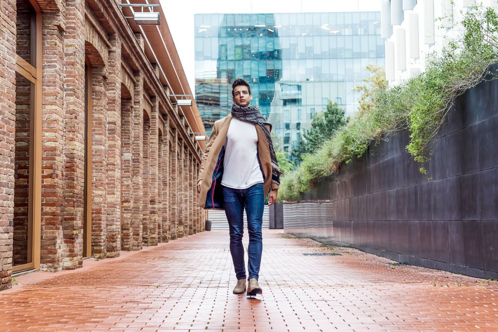 Man wearing camel coat and scarf walking down empty city street
