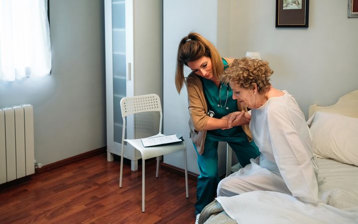 Caregiver helping older patient to get out of bed
