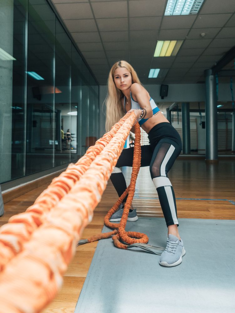 Strong female pulling ropes in gym