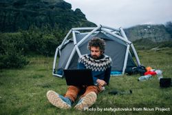 Man working on laptop in front of a campsite 4dXMr4