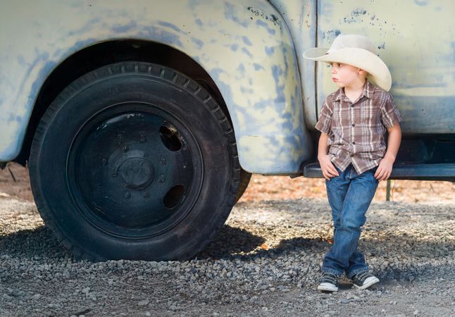 Young Boy Wearing Cowboy Hat Relaxing Leaning Against Antique Truck..