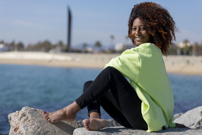 Smiling female sitting on rocks near shoreline in bright green shirt