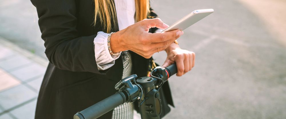 Unrecognizable businesswoman with e-scooter looking at cellphone