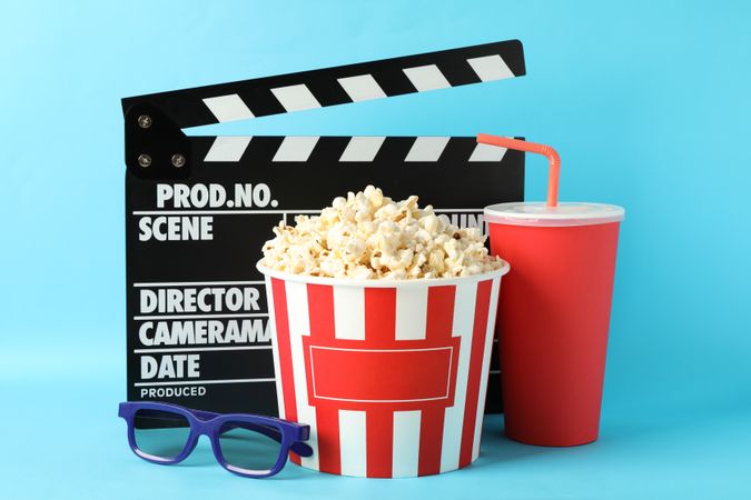 Clapperboard, bucket with popcorn, drink and 3d glasses on blue background