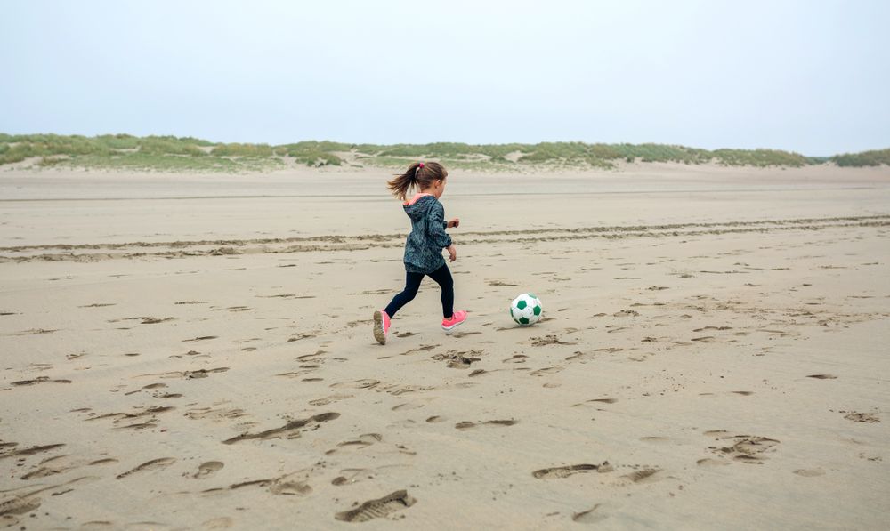 Little girl playing soccer on the beach