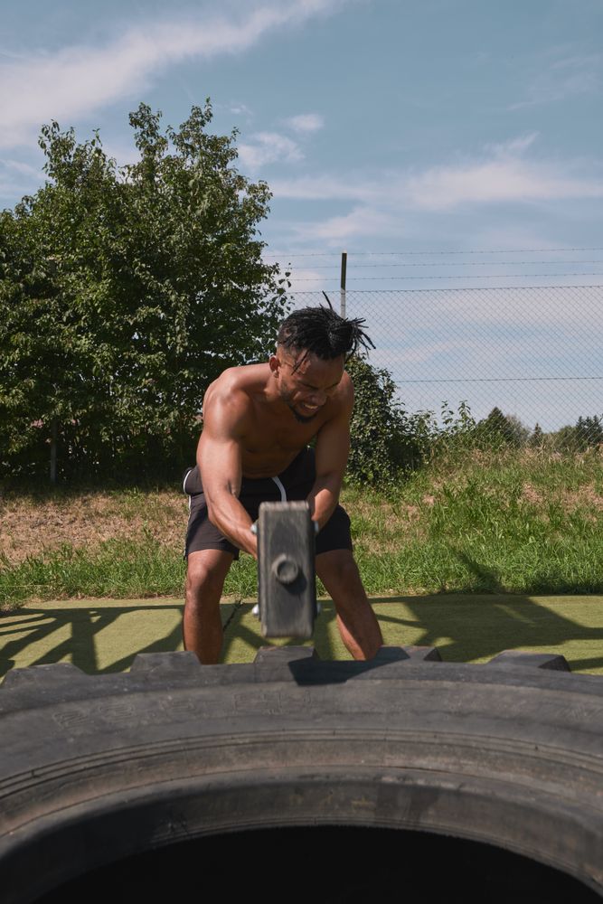 Muscular Black guy hammering tire in outdoor gym