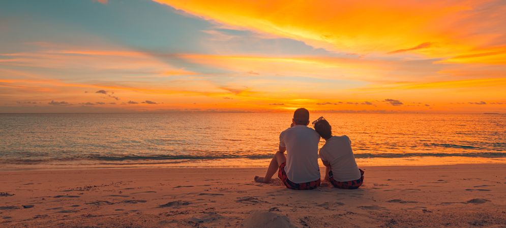 Two people sitting and looking out at the ocean on sunset