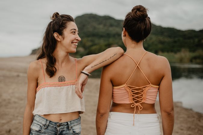 Anonymous tattooed woman leaning on friend on beach