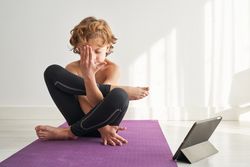 Kid training Pindasana position near tablet at home