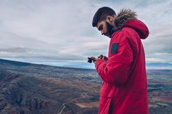 Focused tourist browsing smartphone while standing at mountain top