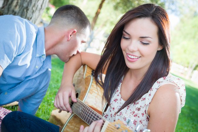 Young Adult Female Playing Guitar with Boyfriend In The Park.