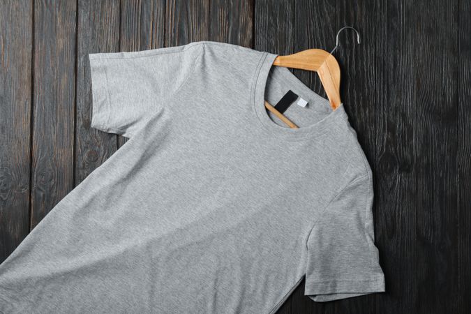 Hanger with blank gray t-shirt on wooden background, space for text