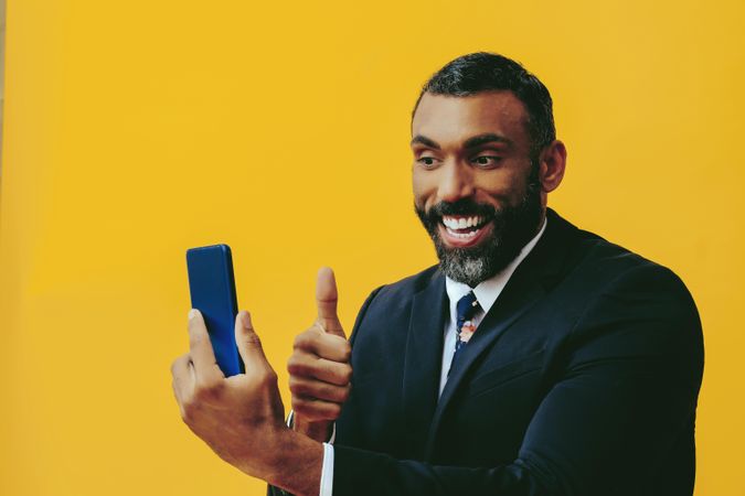 Happy Black businessman in suit speaking at smartphone screen while giving the thumbs up
