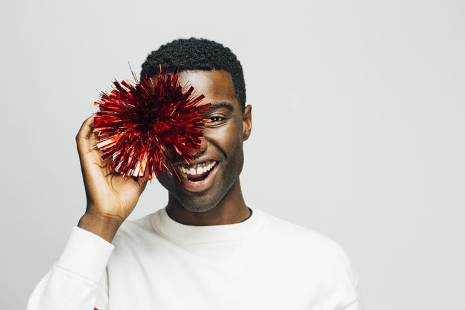 Smiling Black man hiding one eye behind a red pompom