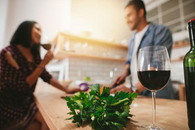 Man and woman talking in the kitchen with glass of wine in focus