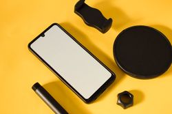 Mock up phone and accessories scattered on yellow table with shadow and space for text
