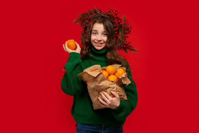 Young girl in green sweater holding paper bag of oranges
