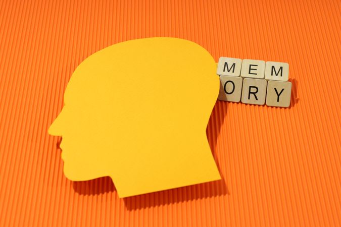 Orange duotone flat lay of head with shadow with the word “memory” in wooden blocks