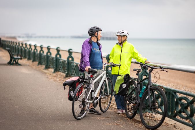 Two older people with bikes talking by the coast