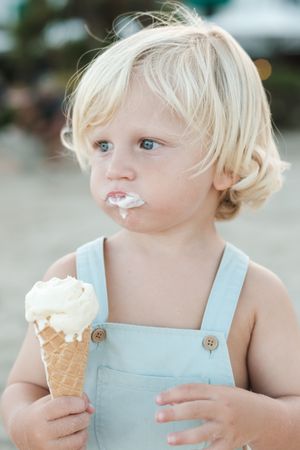 Cute boy with melted ice cream cone on street