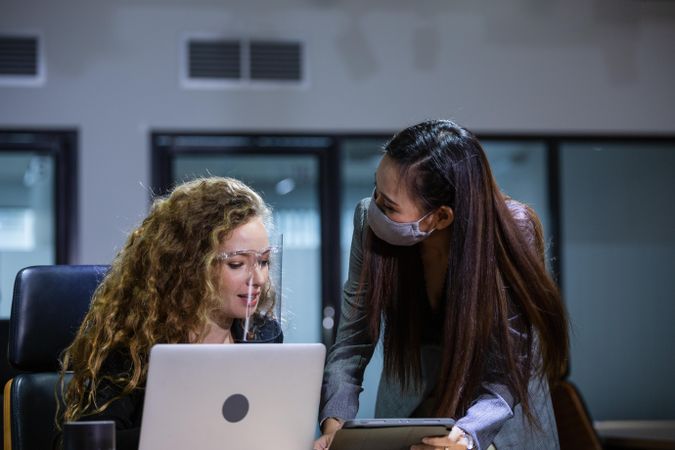 Two female colleagues in covid protecting working together in office