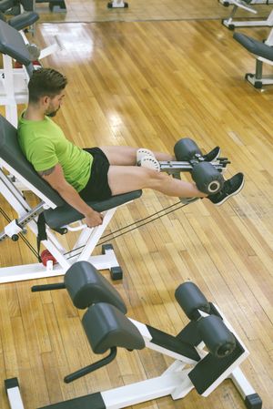Looking down at muscular male in green t-shirt working out quads using leg extension machine