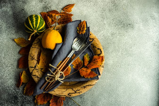 Top view of napkin, cutlery and gourds on wooden bowl and dried fall leaves