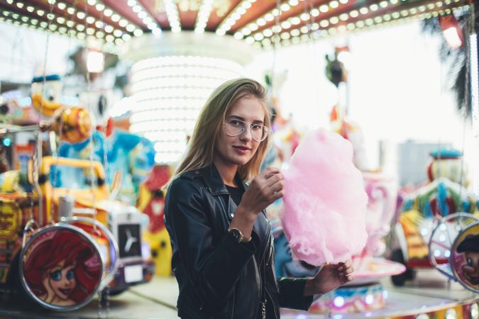 Trendy woman picking at large cotton candy outside of fairground ride