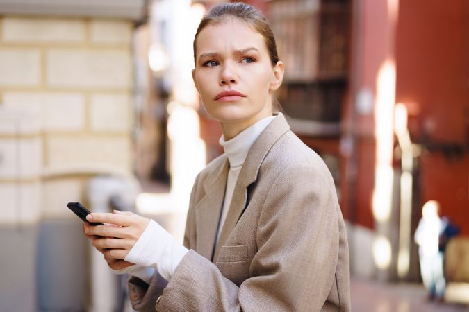 A pensive and contemplative woman found in an urban setting while using her smartphone