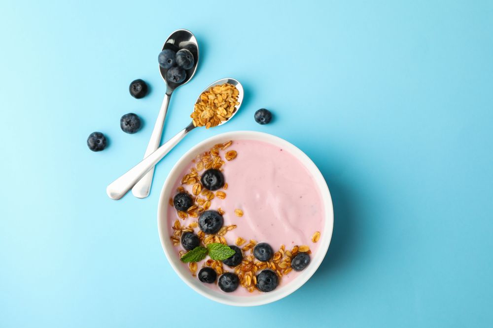 Yogurt with granola, blueberry and mint on color background