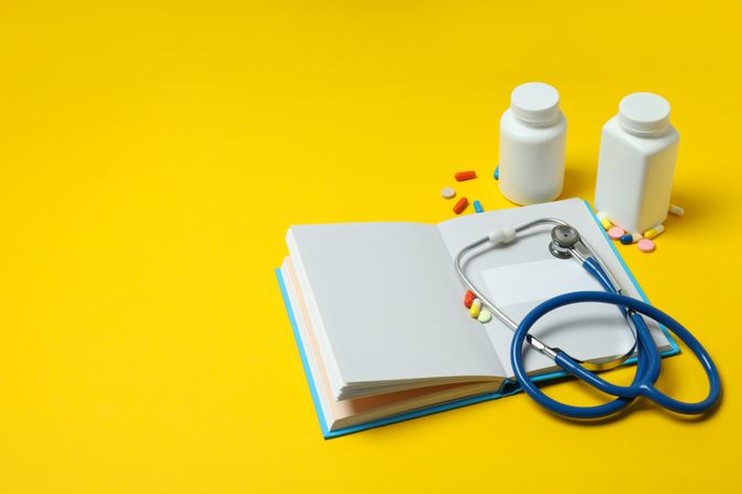 Notepad, stethoscope and jars of pills on yellow background, space for text