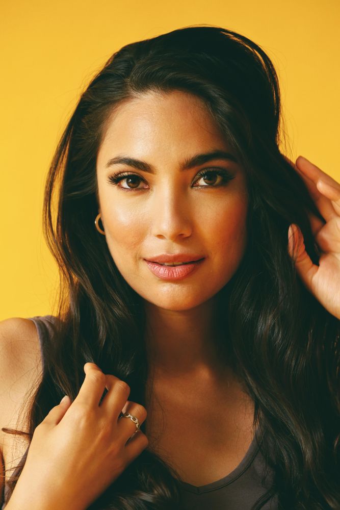 Smiling Hispanic woman looking at camera in yellow room with her hand to her hair