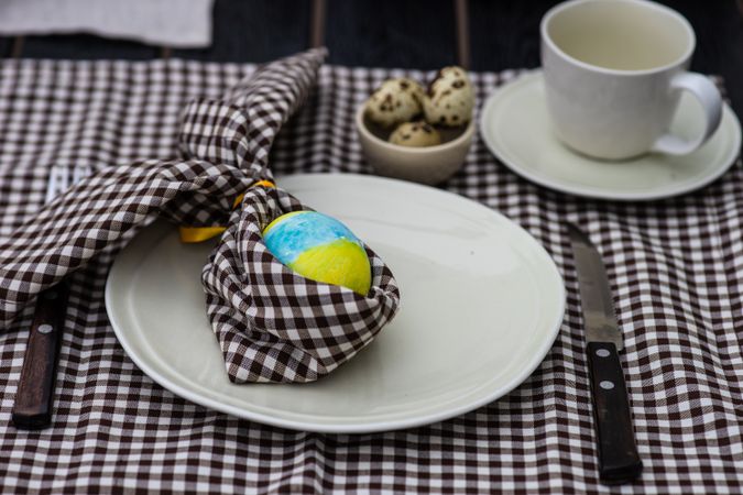 Easter table setting with checkered brown napkin and blue and yellow decorative egg