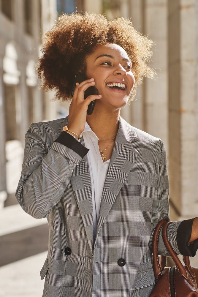Cheerful Black woman speaking on smartphone on city s