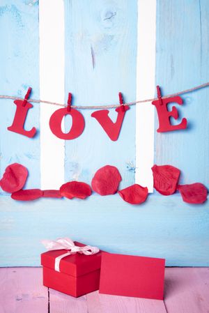 Red gift box with blank message card and the word love written in paper letters hanging on twine
