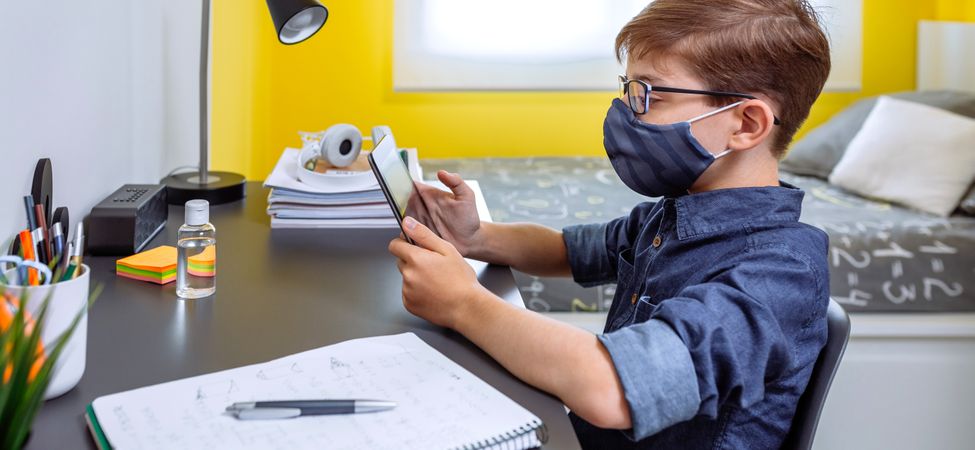 Boy with face mask doing homework with a tablet