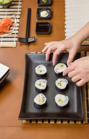 Top view of chef placing sushi rolls with rice, avocado and shrimps on rectangular plate
