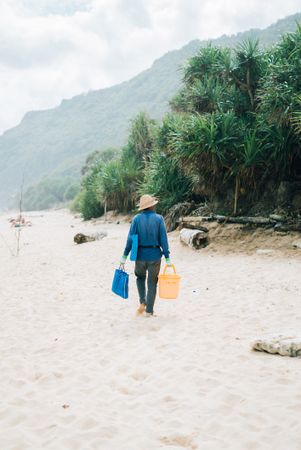 Back of man walking on beach with bucket and bag