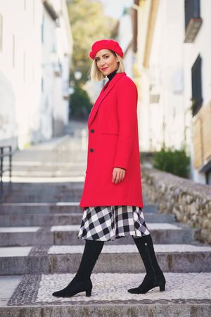 Full body of female in stylish red outfit looking back while walking on stone steps on streets