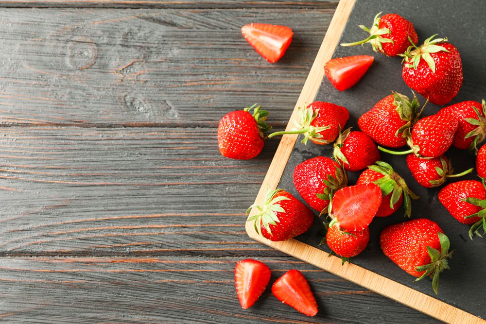 Cutting board and fresh strawberries on wooden table, top view and space for text. Summer sweet fruits and berries