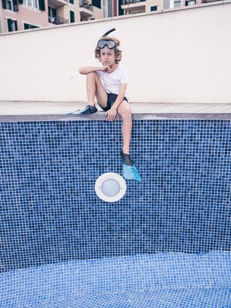 Sad preteen boy sitting on side of empty pool