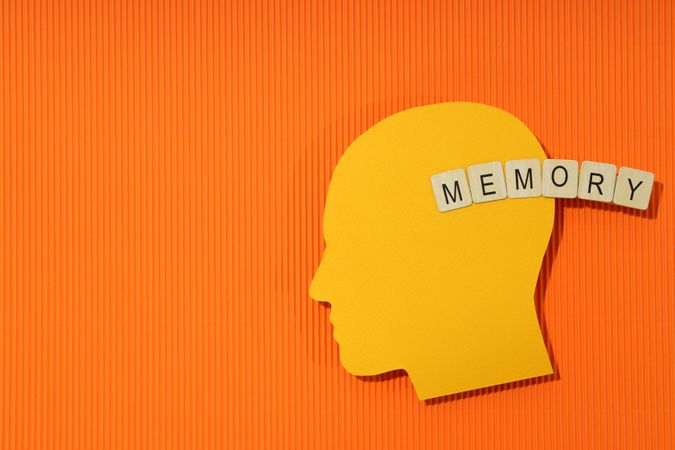 Orange duotone flat lay of head with the word “memory” in wooden blocks, copy space