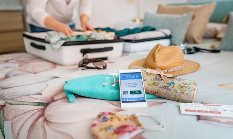Cell phone with covid passport with unrecognizable woman preparing suitcase for vacation