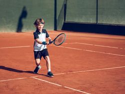 Adorable little boy running to hit ball while playing tennis