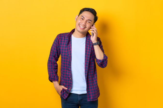 Asian male smiling and talking on cell phone in yellow studio shoot
