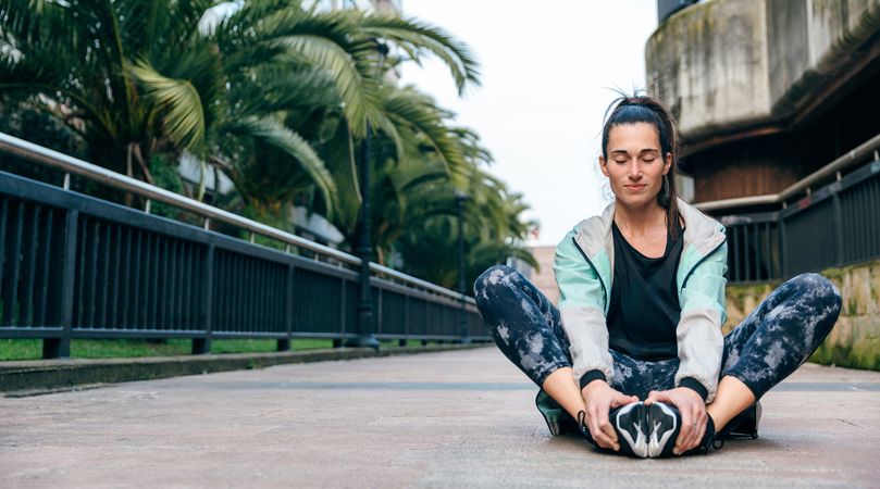 Woman stretching legs while sitting on the floor holding her feet with space for text