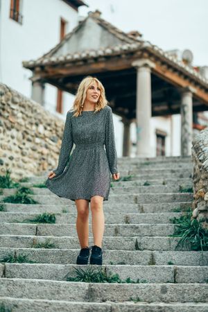 Smiling blonde woman wearing dress walking down cement staircase outside