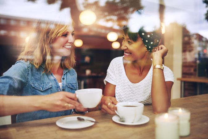 Two female friends sitting at a cafe table chatting and laughing