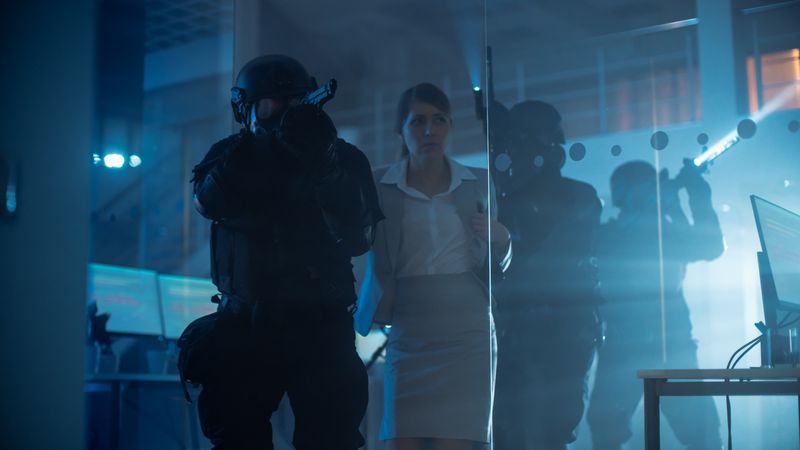 Masked Squad of Armed SWAT Police Officers Rescue a Female Hostage in a Dark Seized Office Building with Desks and Computers.